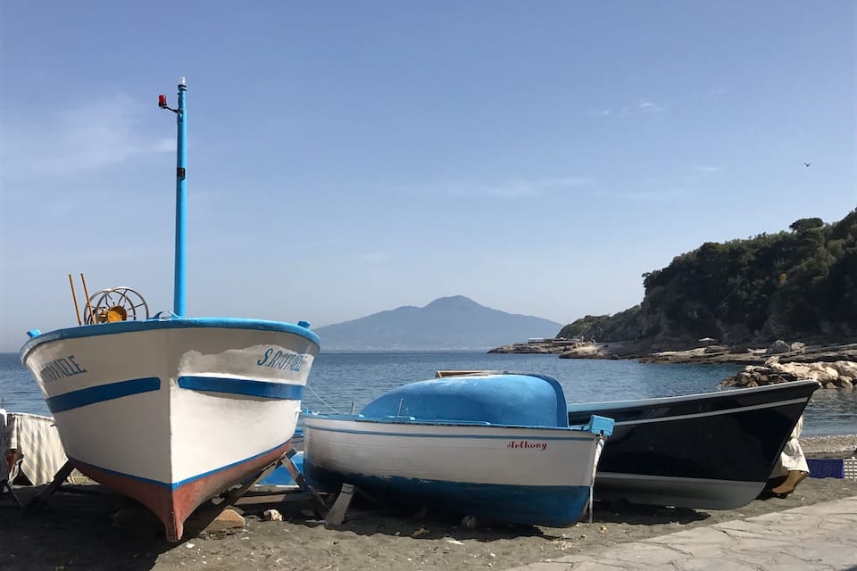 Three boats docked at a rocky shore with a mountain in the background.