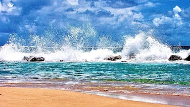 A beach with waves crashing against rocks and a clear blue sky.