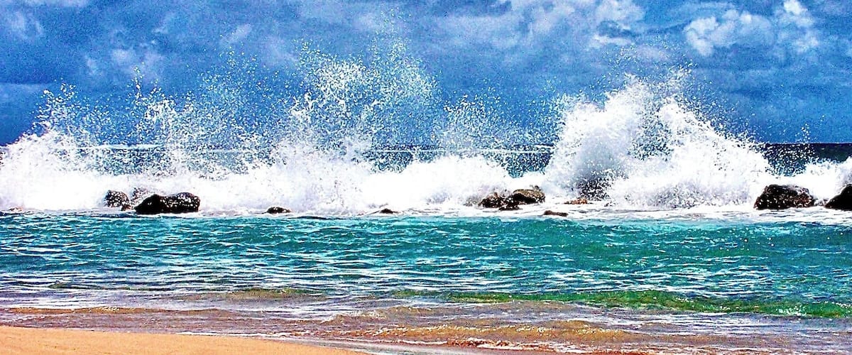 A beach with waves crashing against rocks and a clear blue sky.