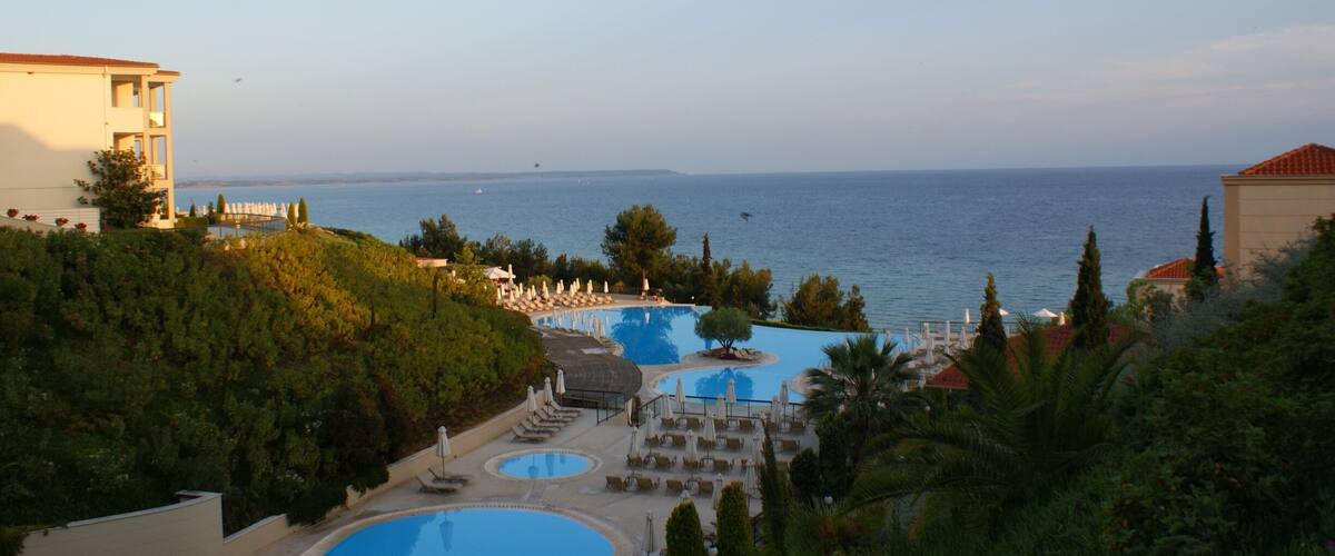 A resort with a large swimming pool, lounge chairs, and a view of the sea.