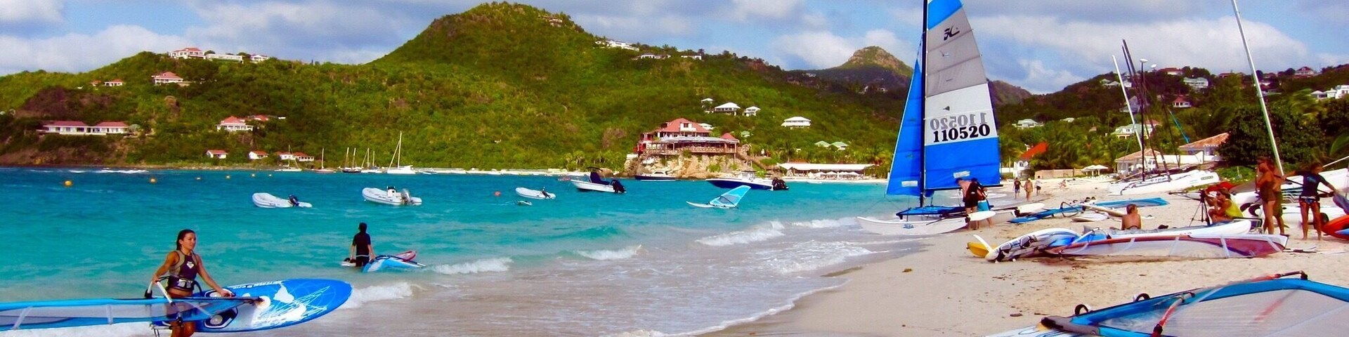 Una playa con veleros, una orilla arenosa y una colina al fondo.
