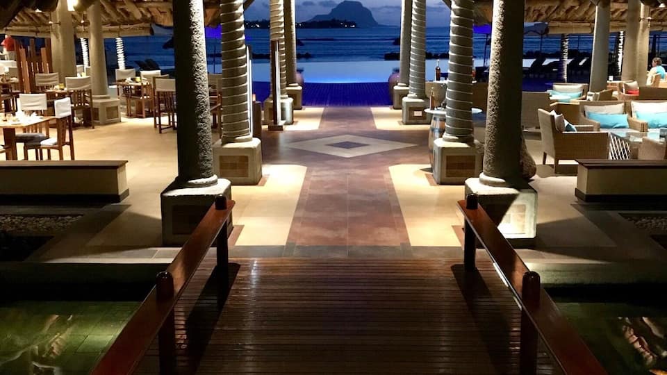 A wooden deck leading to a beach with a thatched roof structure and seating areas.