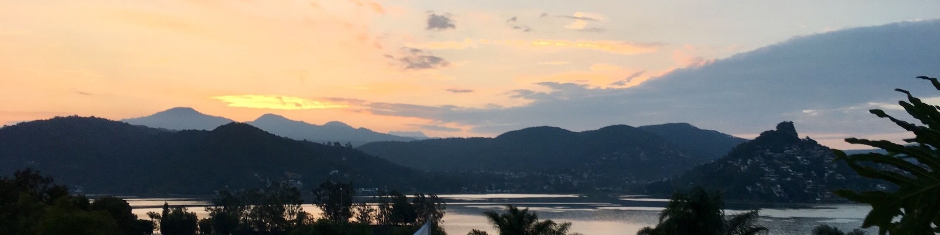 Um pôr do sol sobre um lago, com montanhas ao fundo.