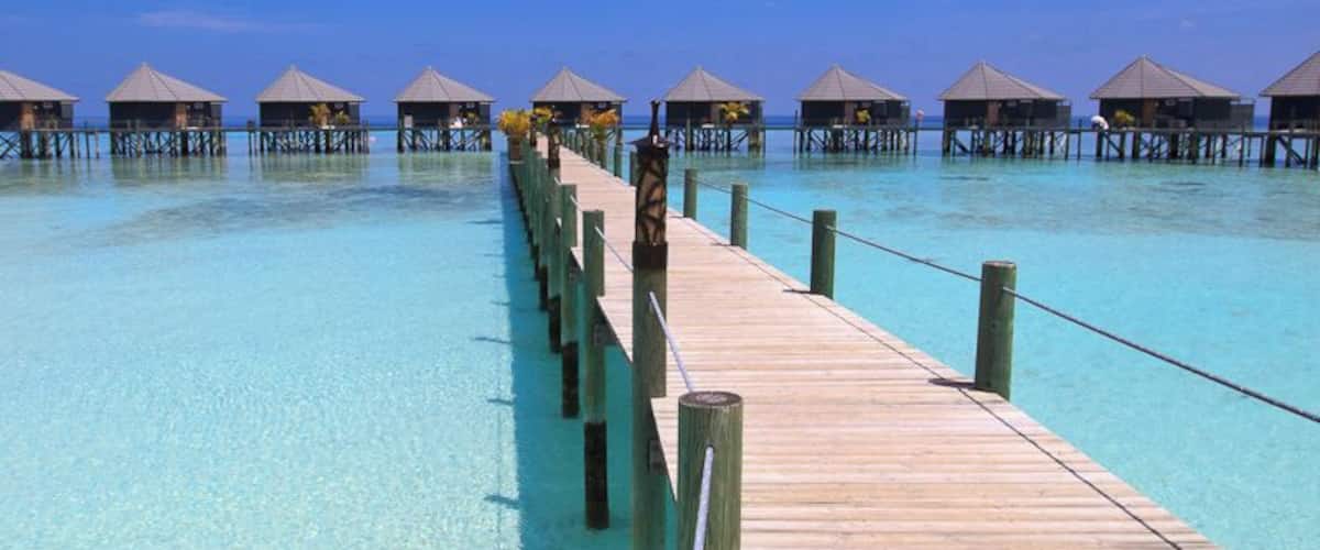 A wooden pier extending into clear turquoise water, leading to overwater bungalows.