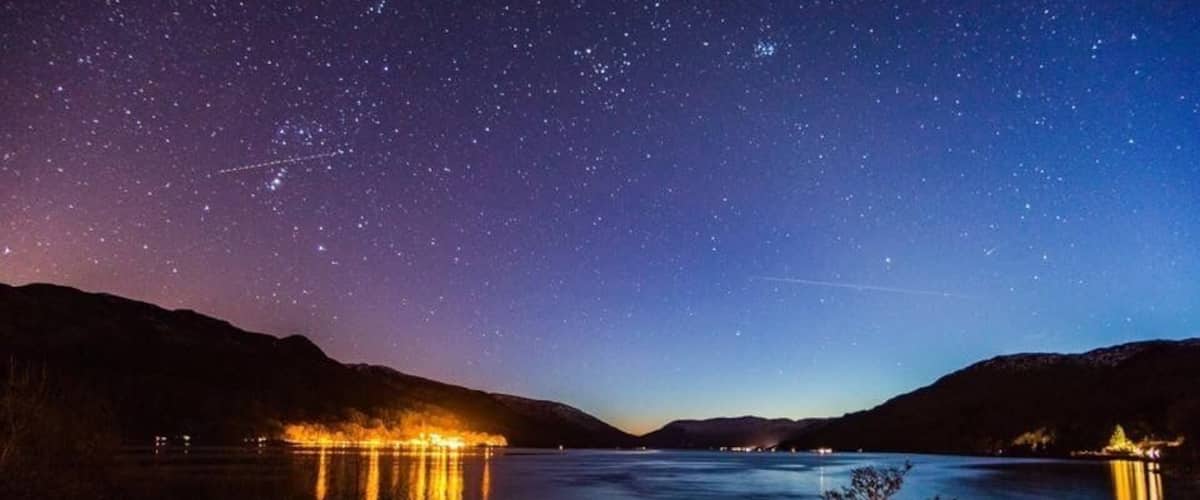 A starry night over a calm lake with mountains in the background.