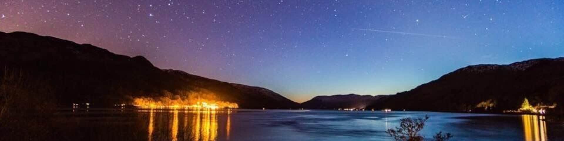 Uma noite estrelada sobre um lago calmo, com montanhas ao fundo.