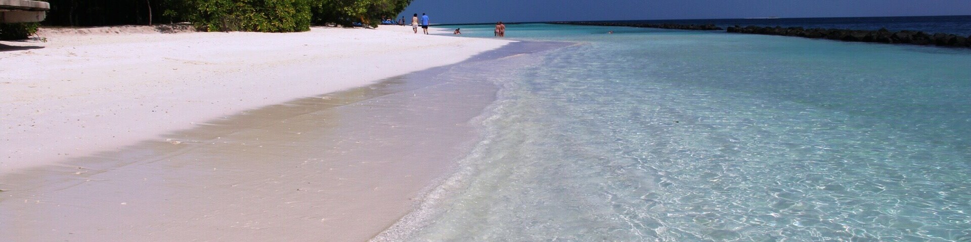 Uma praia com águas turquesa cristalinas, areia branca e vegetação verde exuberante.