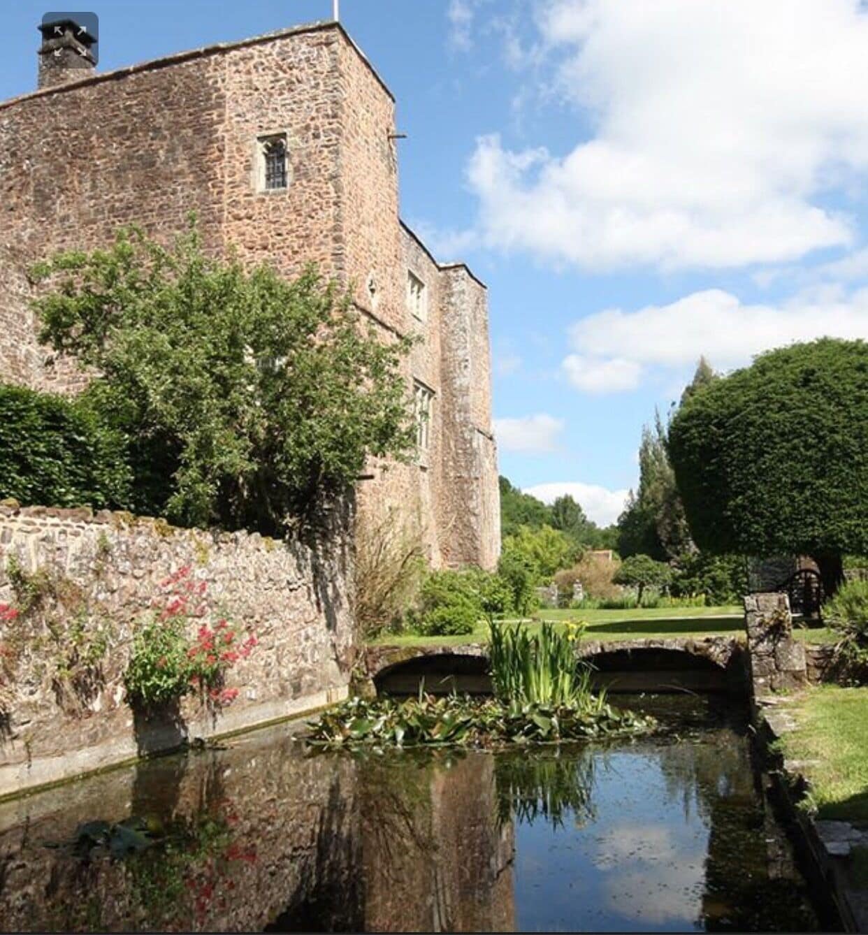 A stone building with a tower, a small bridge, and a pond with lily pads.