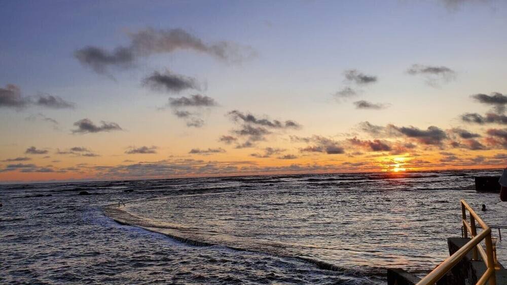 Un coucher de soleil sur l’océan, avec une jetée en bois et des vagues.