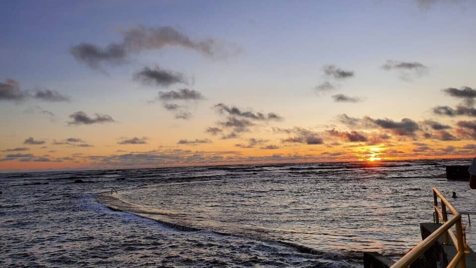A sunset over the ocean with a wooden pier and waves.