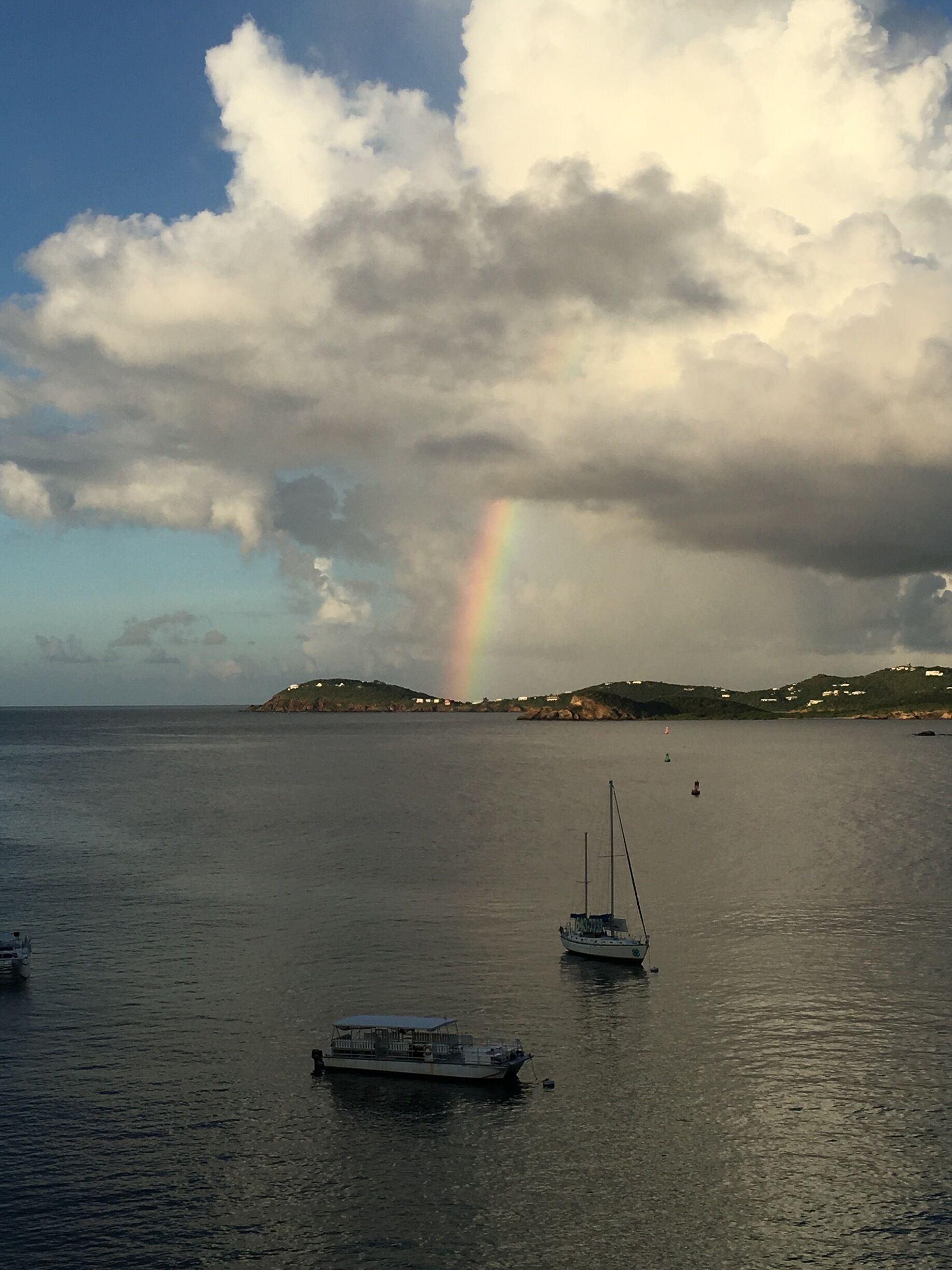 A calm sea with boats, a rainbow, and a cloudy sky.