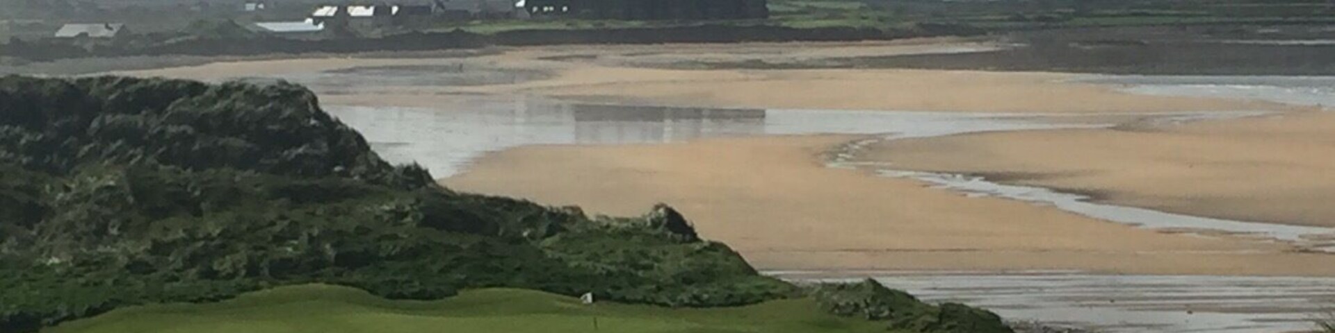 Un paysage côtier avec un château, des collines verdoyantes et une plage de sable.