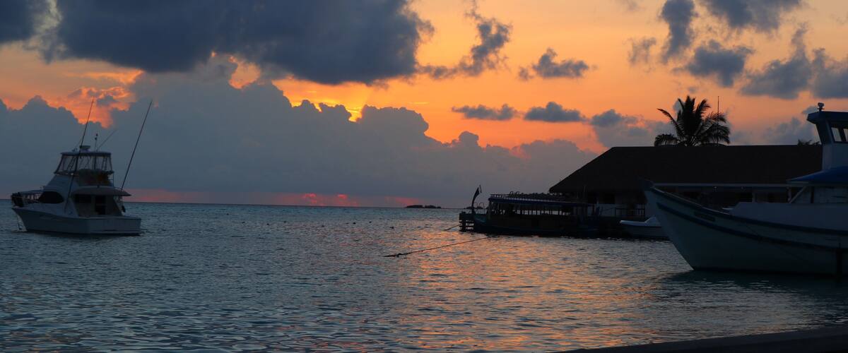 A sunset over a calm sea with boats docked at a pier.