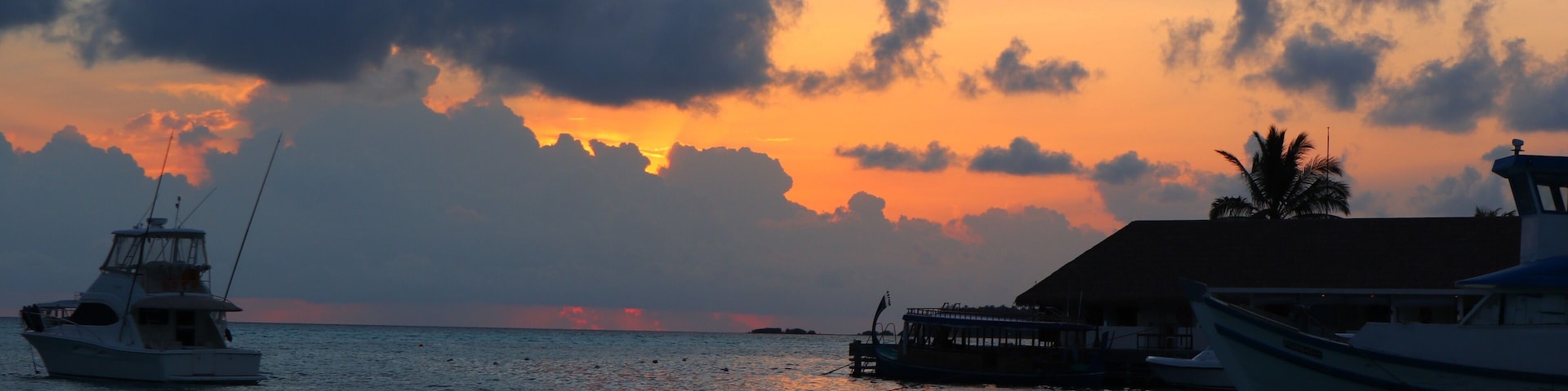 Um pôr do sol sobre um mar calmo, com barcos ancorados em um cais.