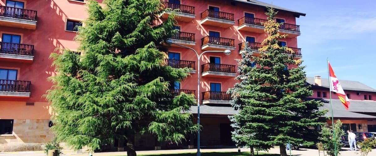A multi-story building with balconies, surrounded by green trees and a clear sky.