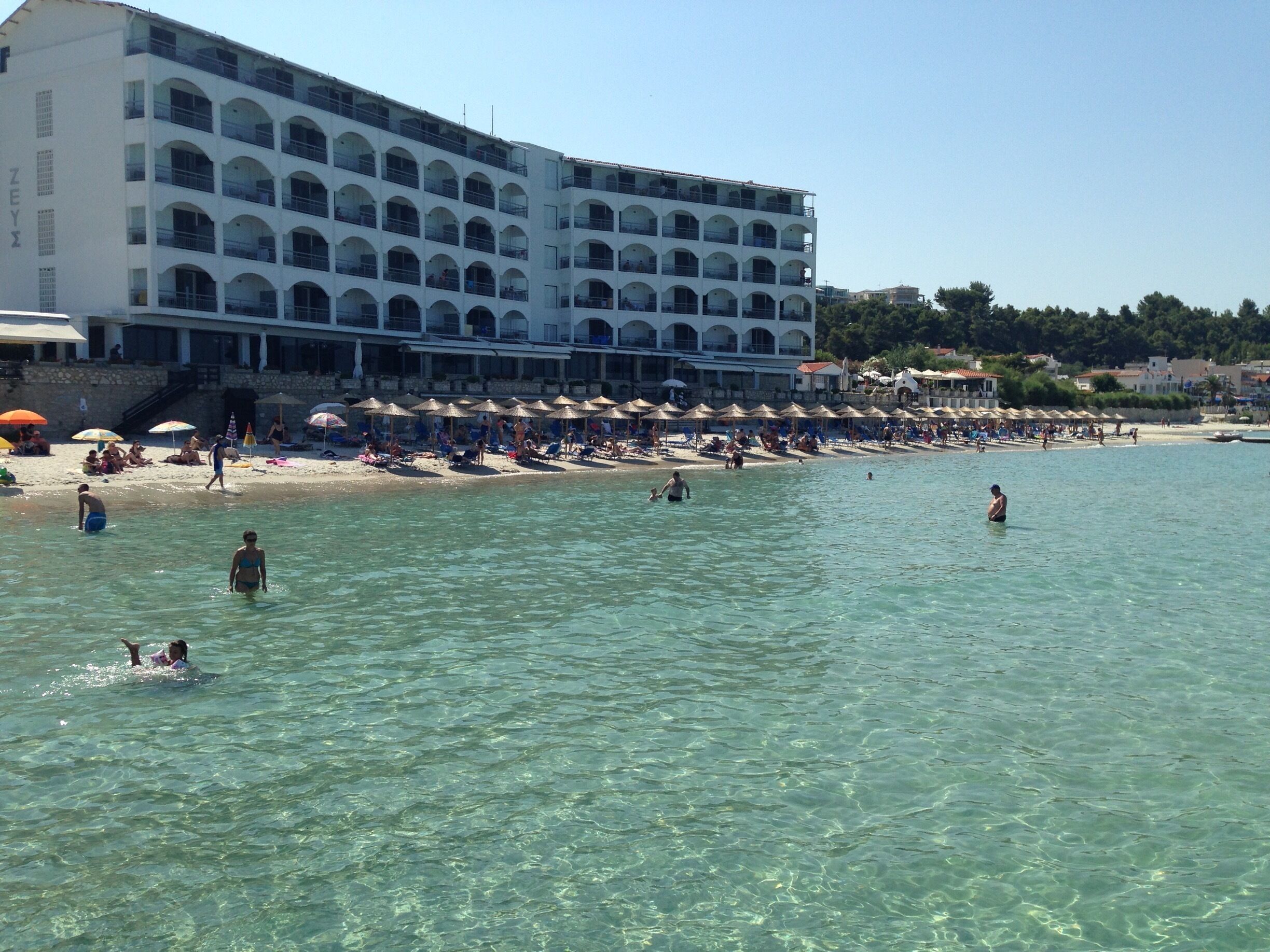 A beach with clear water, umbrellas, and a large hotel building.