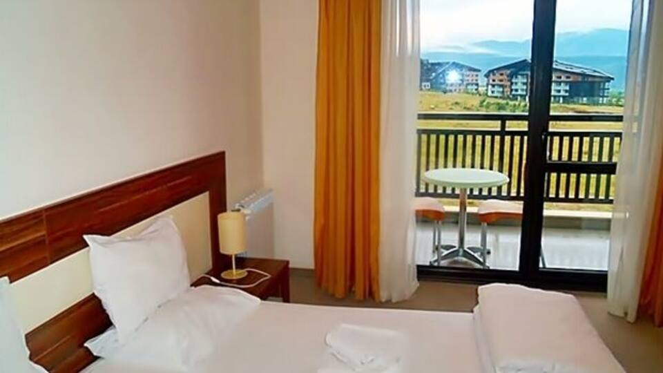 A hotel room with a bed, a nightstand, a lamp, and a balcony with a table and chairs.