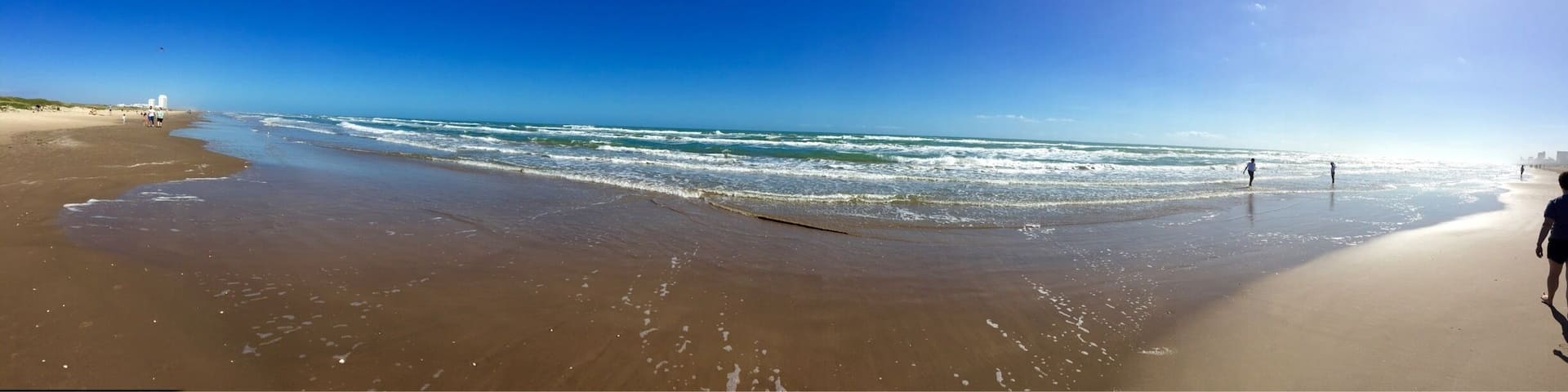 A wide sandy beach with gentle waves and a clear blue sky.