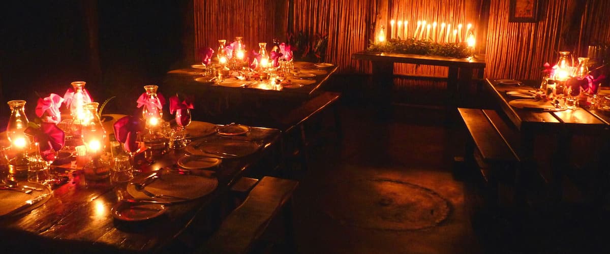 A dimly lit restaurant with wooden tables and chairs, candles, and pink flowers.