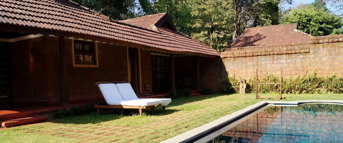 A brick house with a tiled roof, a swimming pool, and a lawn with a lounge chair.