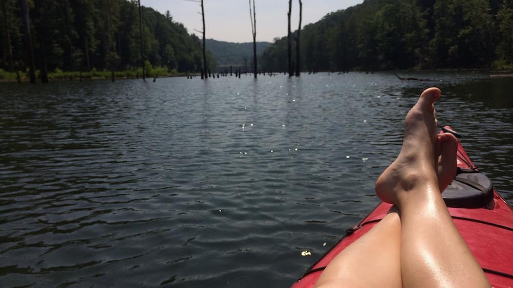 Une rivière paisible où flotte un kayak rouge, bordée de rives boisées.