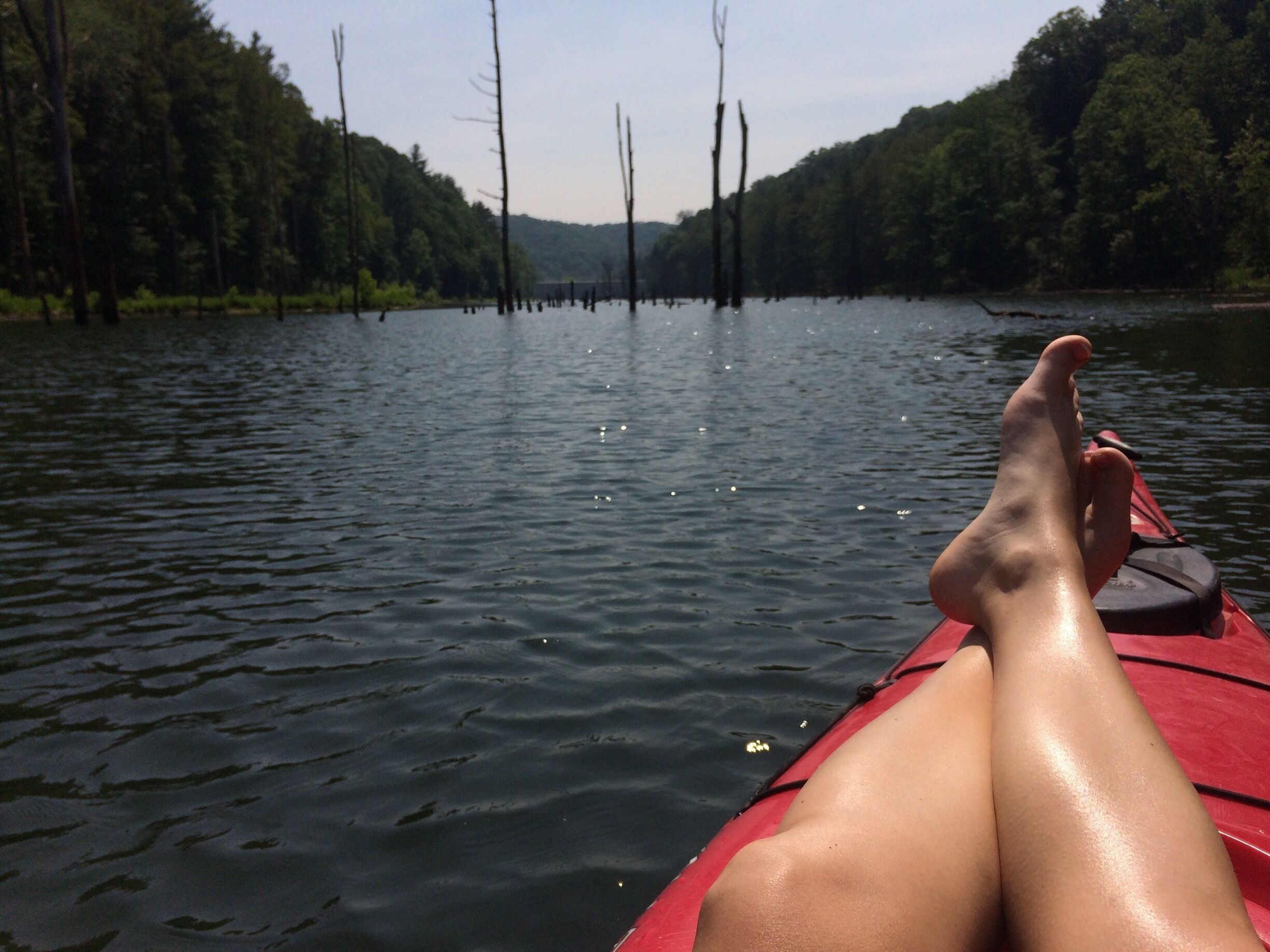 A calm river with a red kayak, surrounded by forested banks.