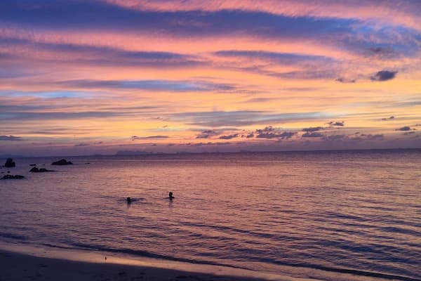 A beach at sunset with a clear sky and calm sea.