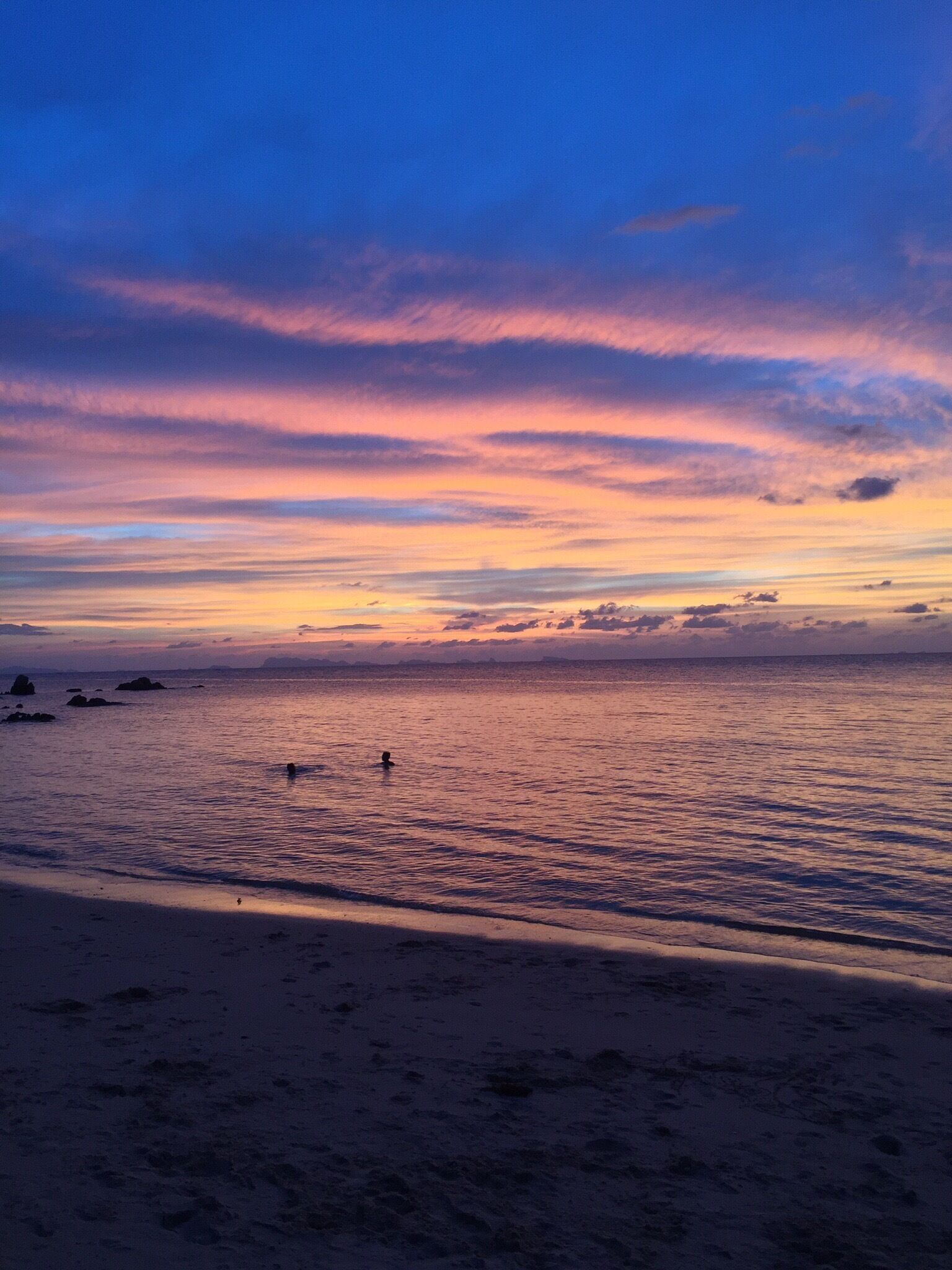 A beach at sunset with a clear sky and calm sea.
