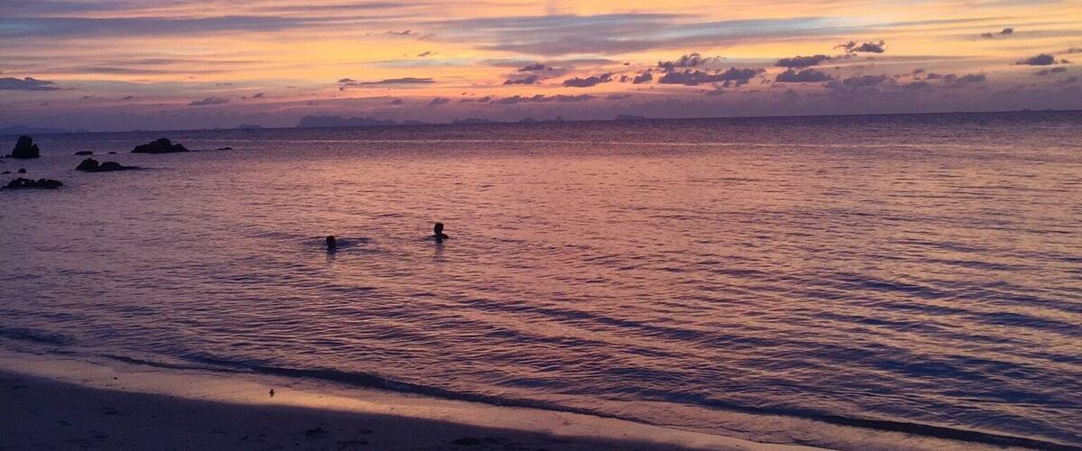 A beach at sunset with a clear sky and calm sea.