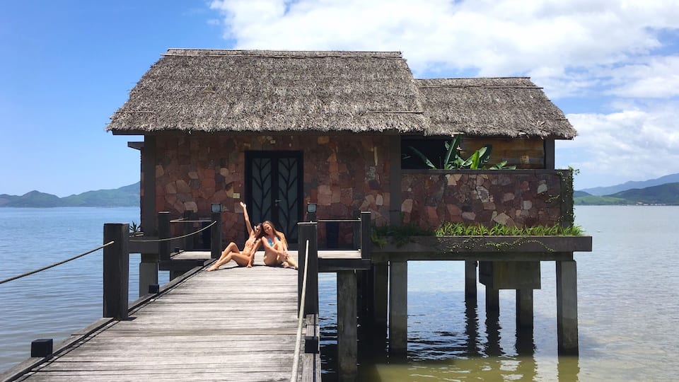 A wooden pier leading to a stone building with a thatched roof.