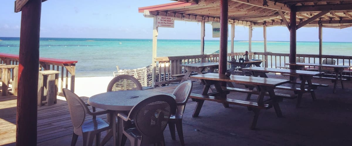 A wooden deck with picnic tables and chairs overlooking a beach.
