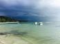 A beach with clear turquoise water, boats, and a forested coastline.