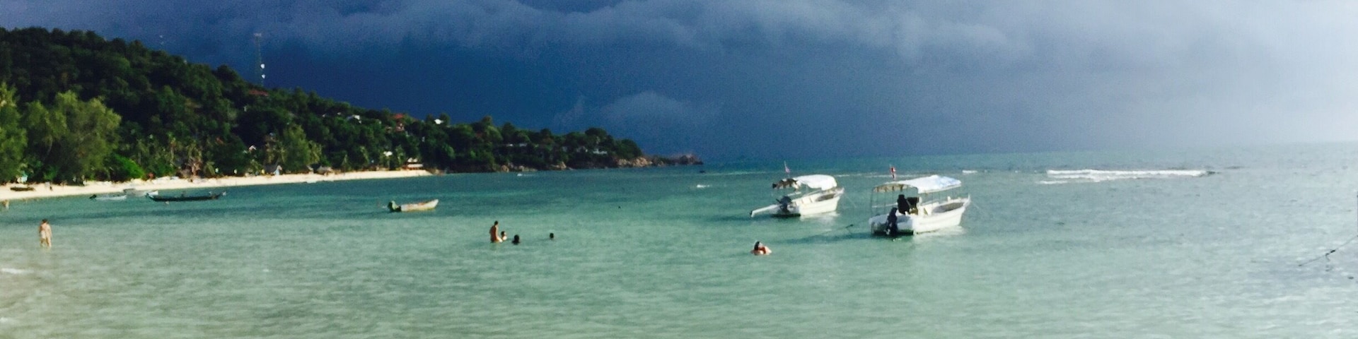 Una playa con aguas turquesas cristalinas, embarcaciones y una costa cubierta de bosque.
