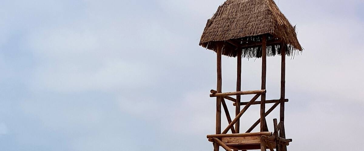 A wooden lifeguard tower on a beach with turquoise water and a clear sky.