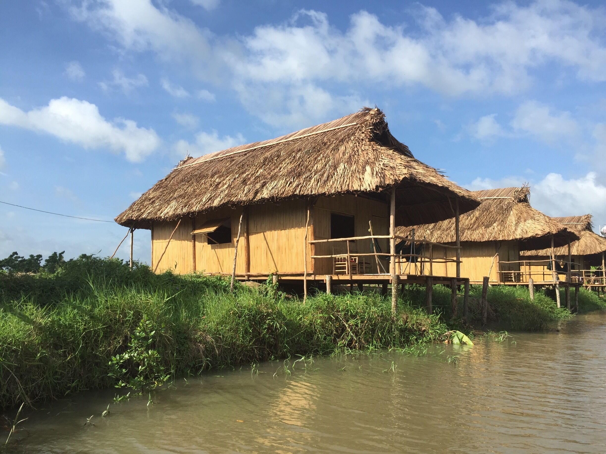 A thatched-roof house by a calm river.