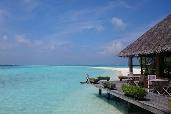Un bungalow en bois, construit sur pilotis au-dessus de l’eau, avec un toit de chaume et une vue sur des eaux turquoise.