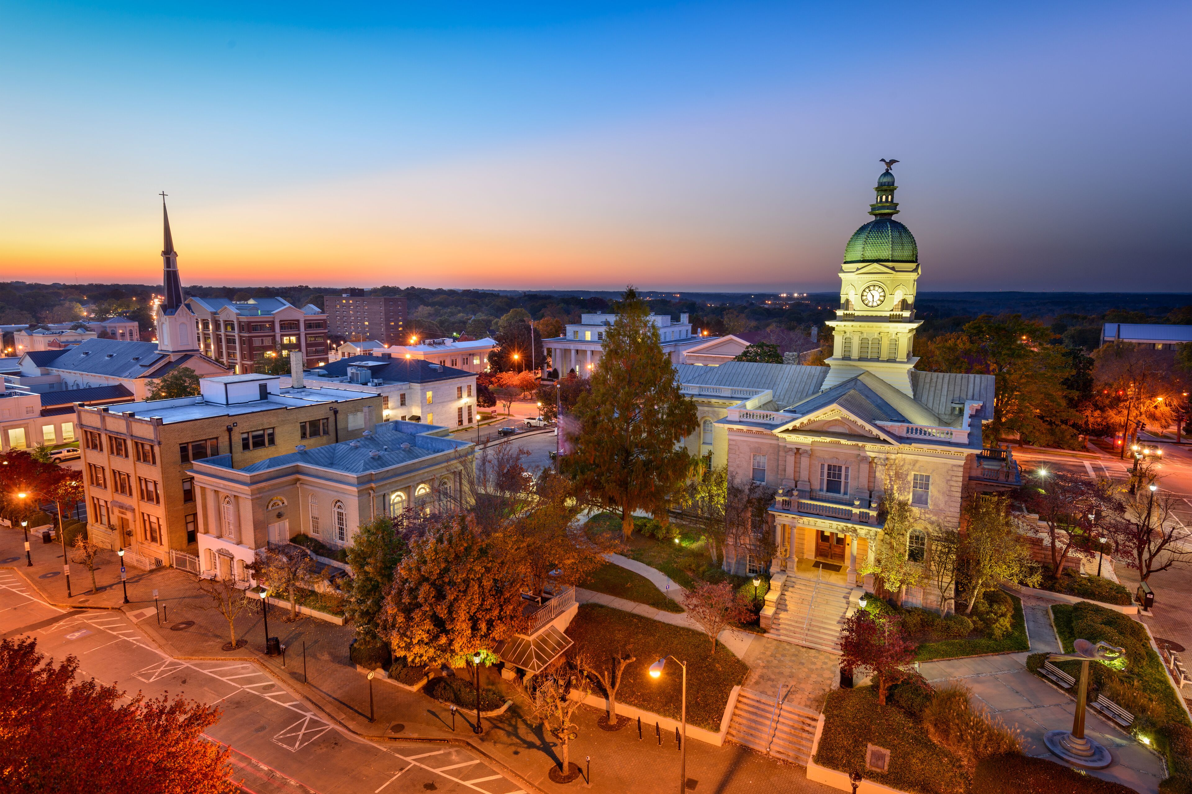 A cityscape at dusk with illuminated buildings, a prominent church steeple, and a clock tower.