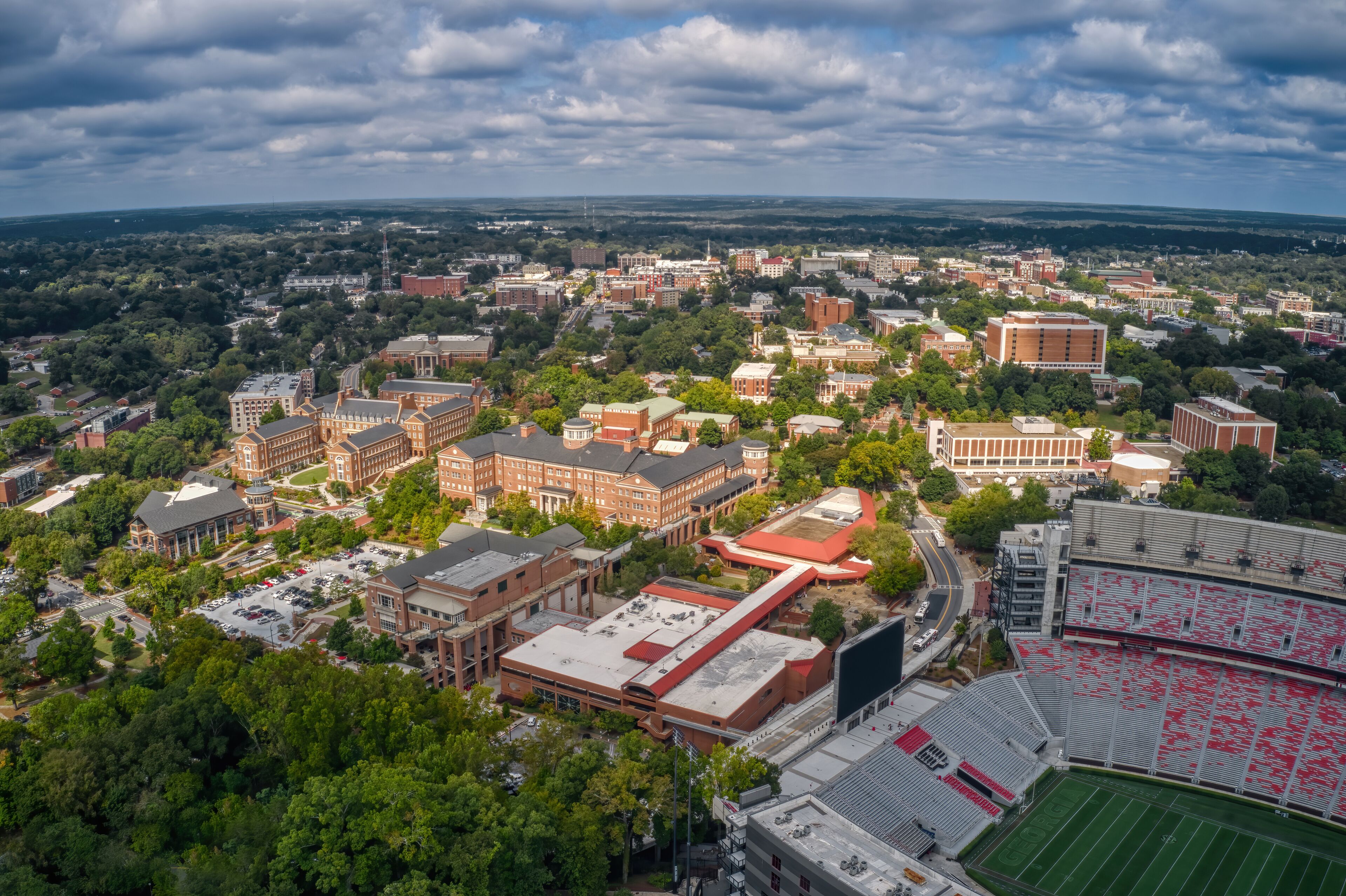An aerial view of a university campus with multiple buildings, a stadium, and surrounding greenery.