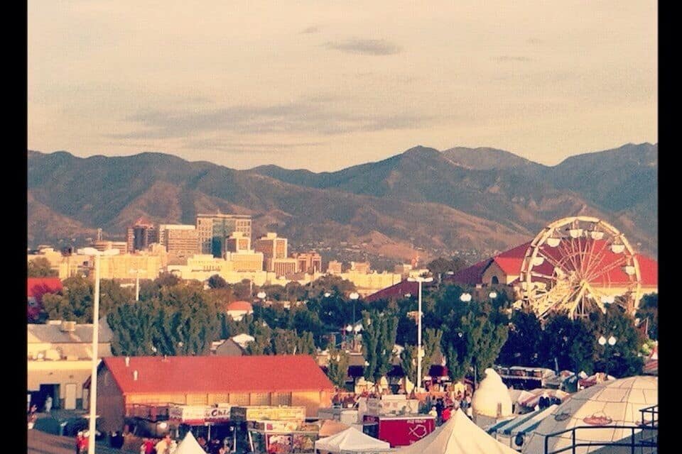Un paisaje urbano con una noria grande, carpas y montañas al fondo.