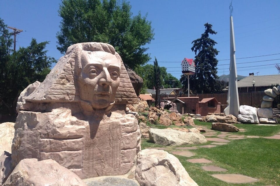 A large stone sculpture of a face, a tall white monument, and a building with a red roof in the background.