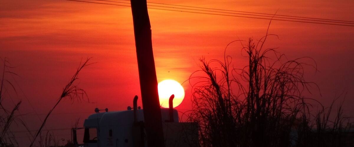 A sunset over a rural landscape with a silhouette of a building and power lines.