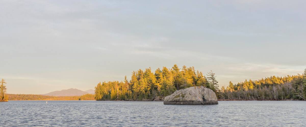 A calm lake with a large rock in the foreground and a forested island in the background.