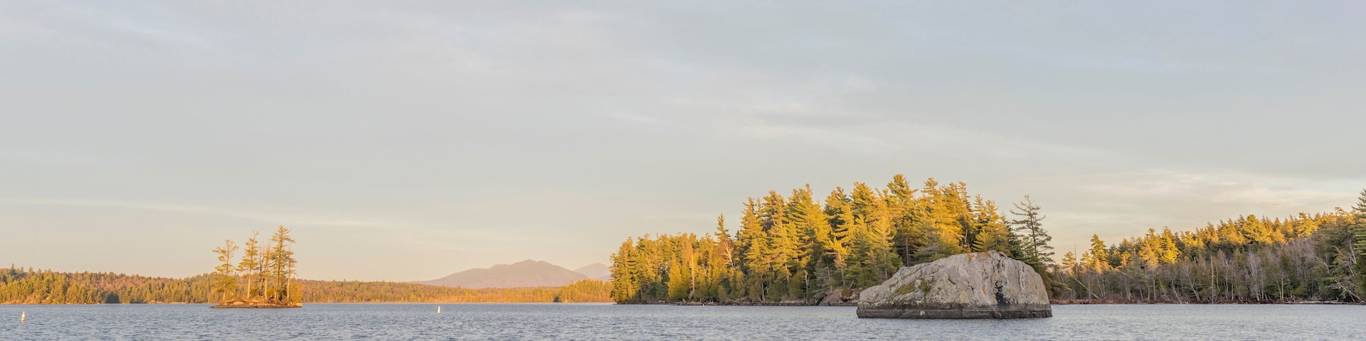 A calm lake with a large rock in the foreground and a forested island in the background.