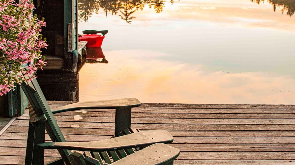 USA, New York. Adirondack Park, Saranac Lake, Hoel Pond, Adirondack chairs on boathouse dock.