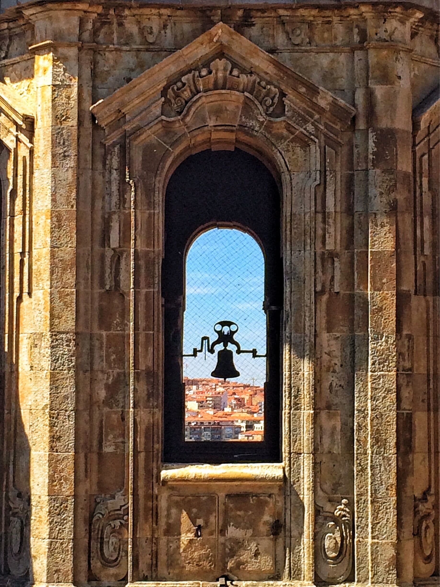 An arched stone window with a bell inside, overlooking a cityscape.