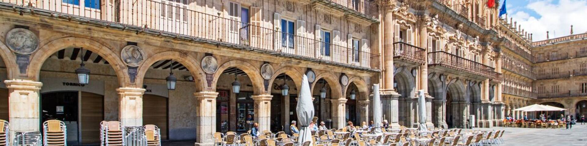 A historic building with ornate architecture, a courtyard with outdoor seating, and flags.