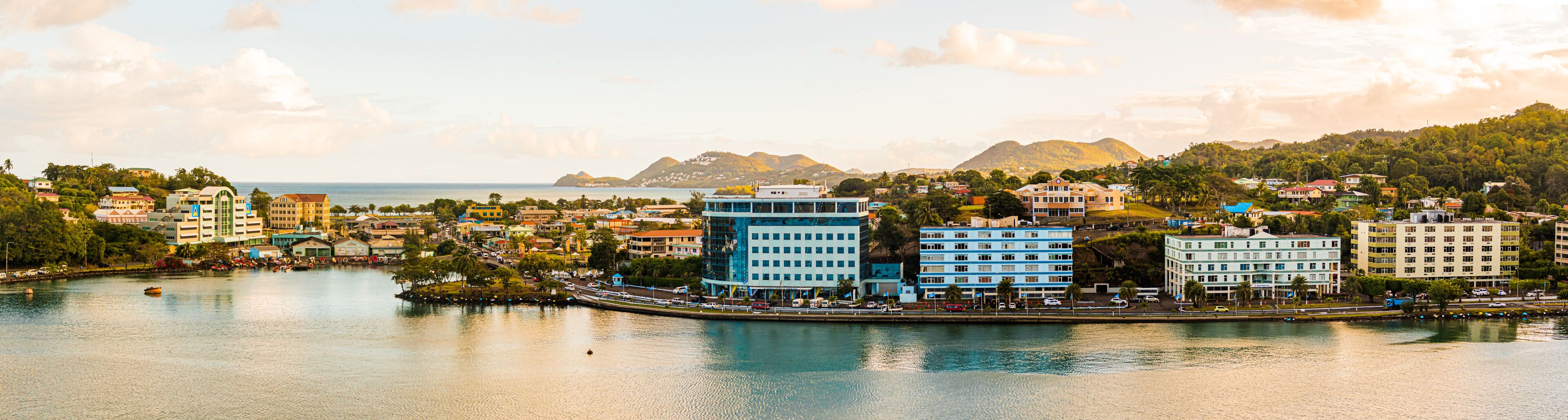 A coastal cityscape with a prominent blue building, a marina, and a mountainous backdrop.