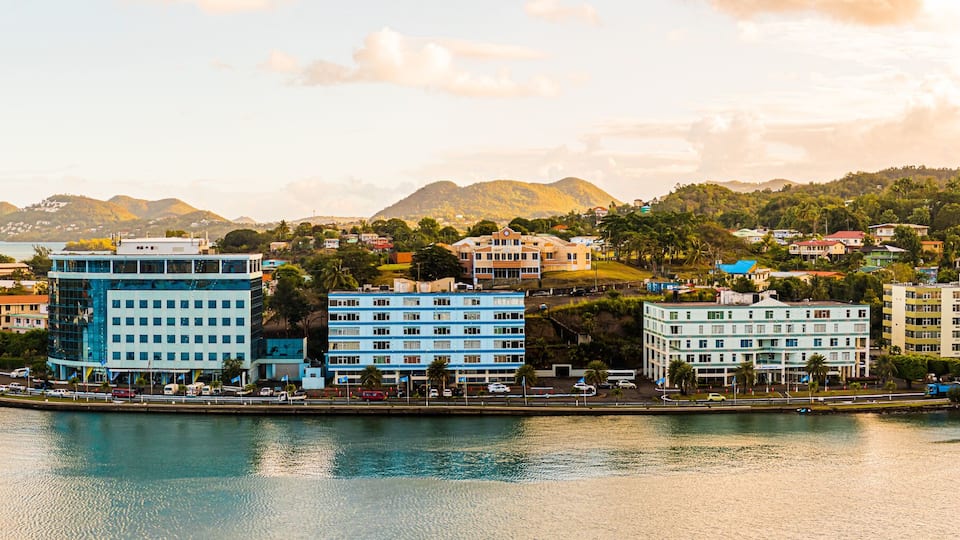 A coastal cityscape with a prominent blue building, a marina, and a mountainous backdrop.