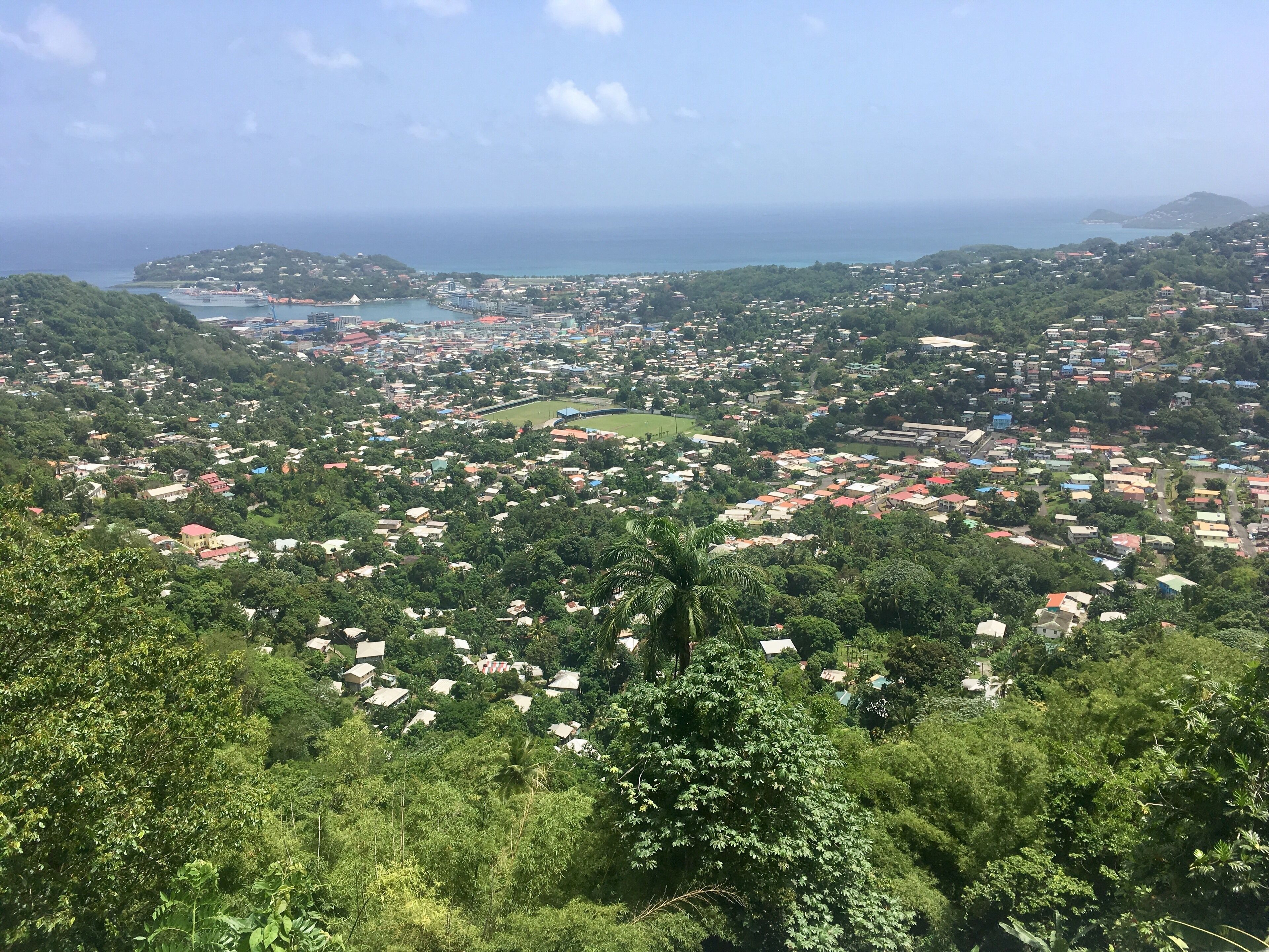 A coastal town with dense housing, green hills, and a view of the sea.