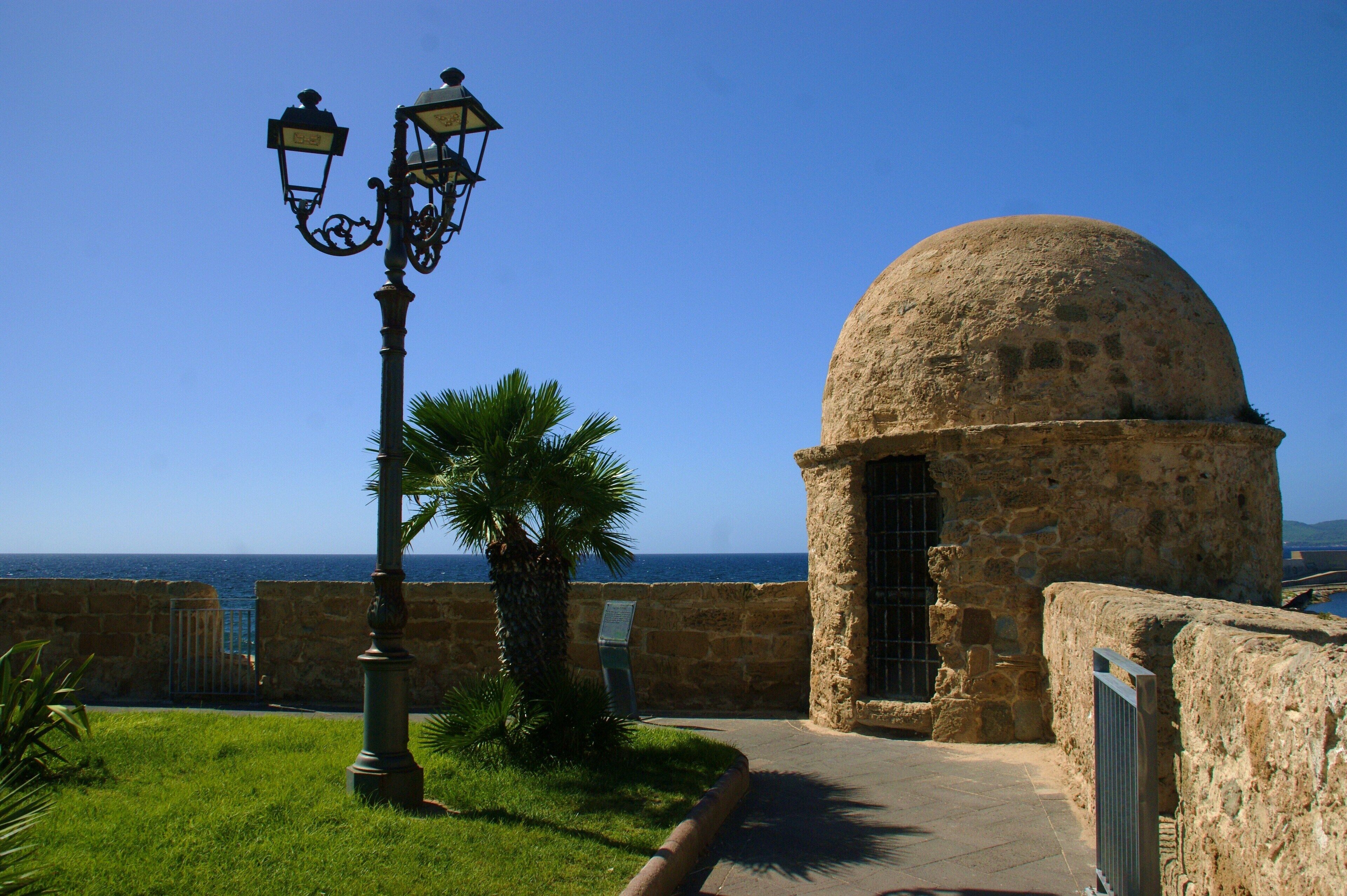 A stone building with a dome, a street lamp, and a palm tree.